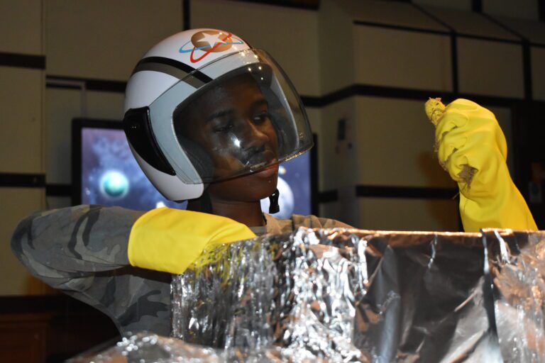 boy wearing space themed helmet with yellow gloves rummaging in tinfoil box