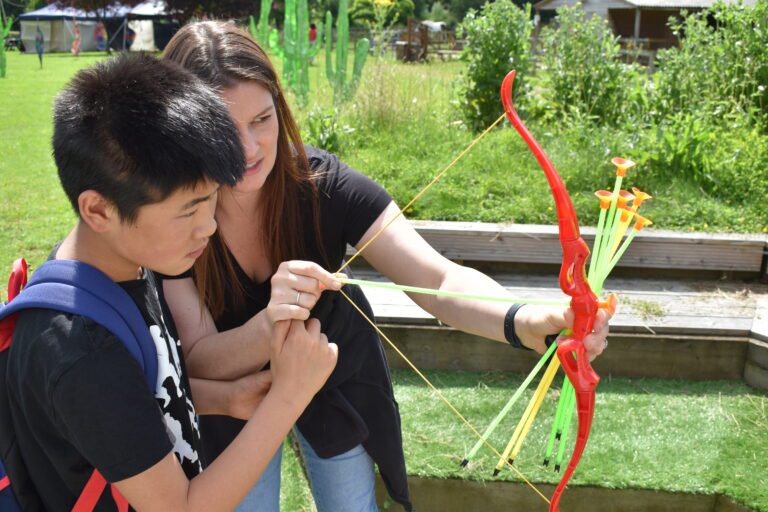 woman showing a boy how to use a toy bow