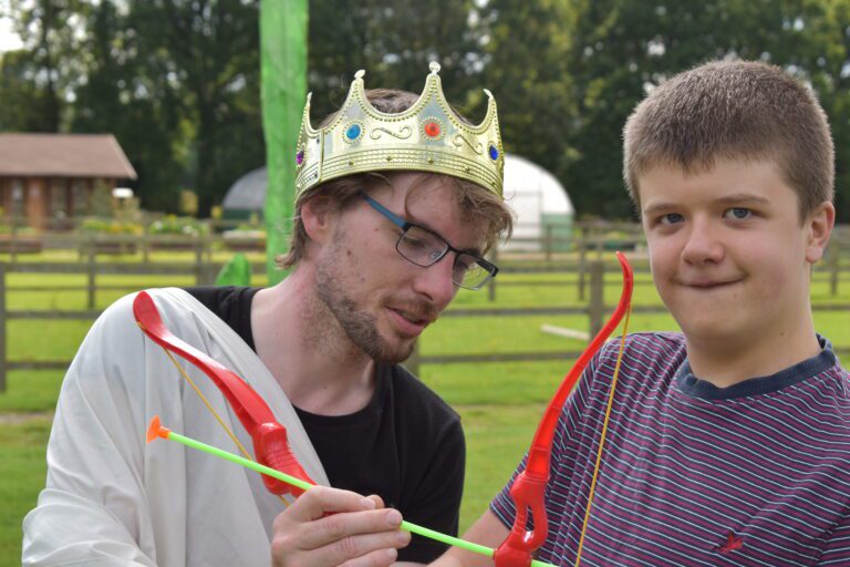 man in crown showing boy how to use a toy bow
