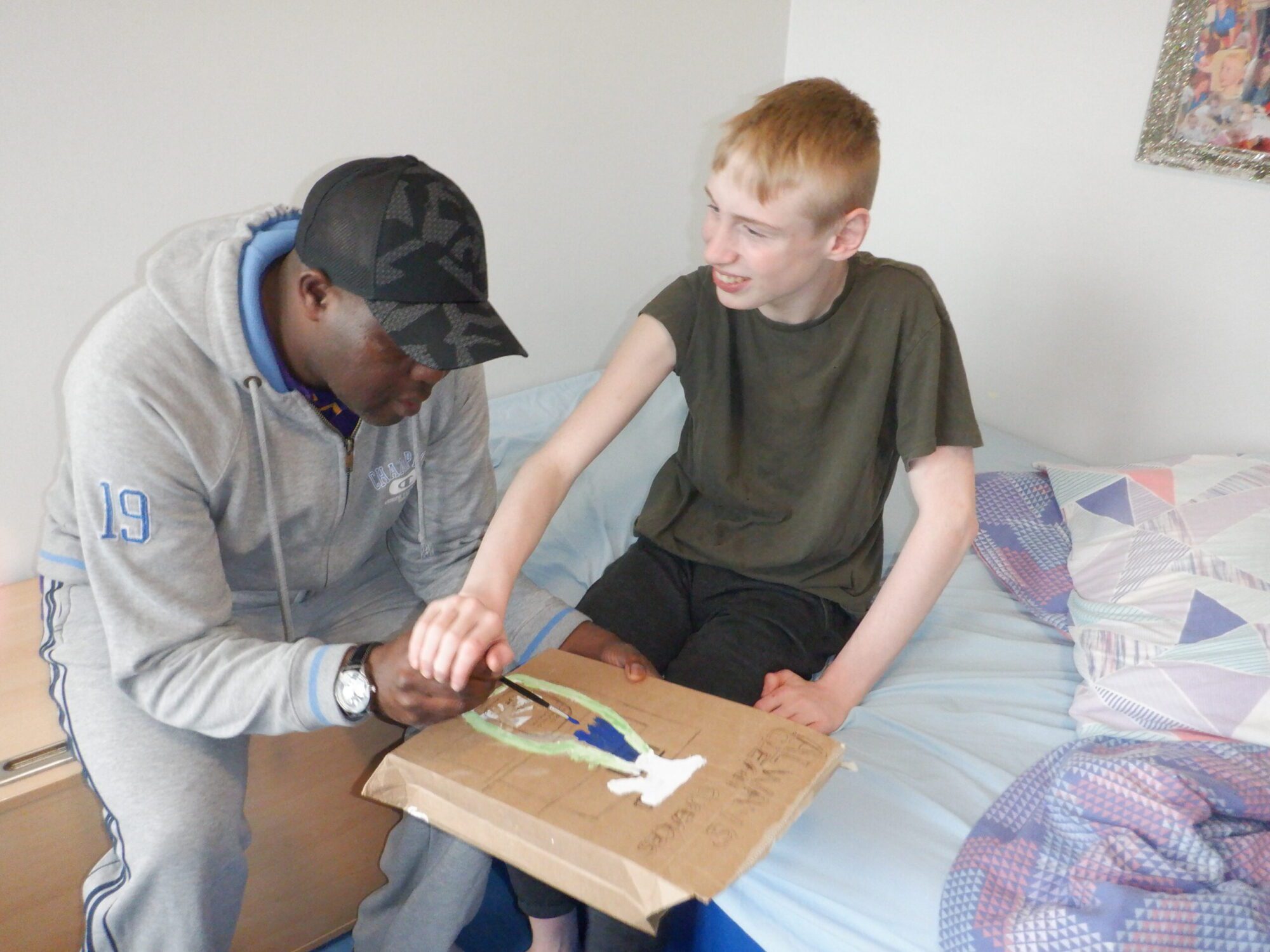 Man helping a boy paint on carboard