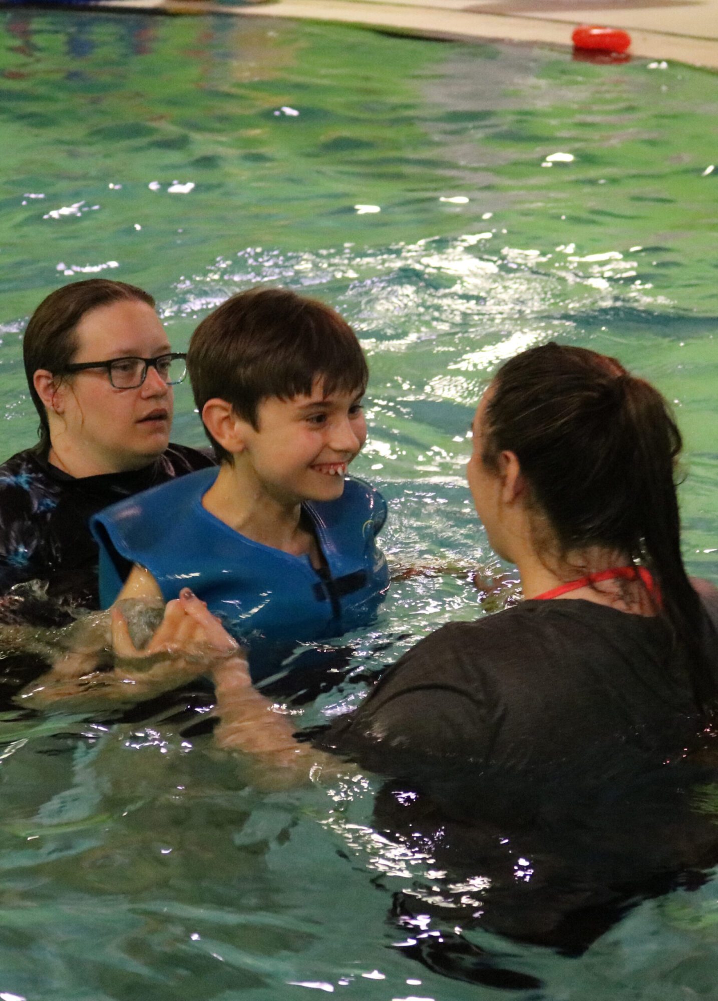 two women holding a boy while he floats in water